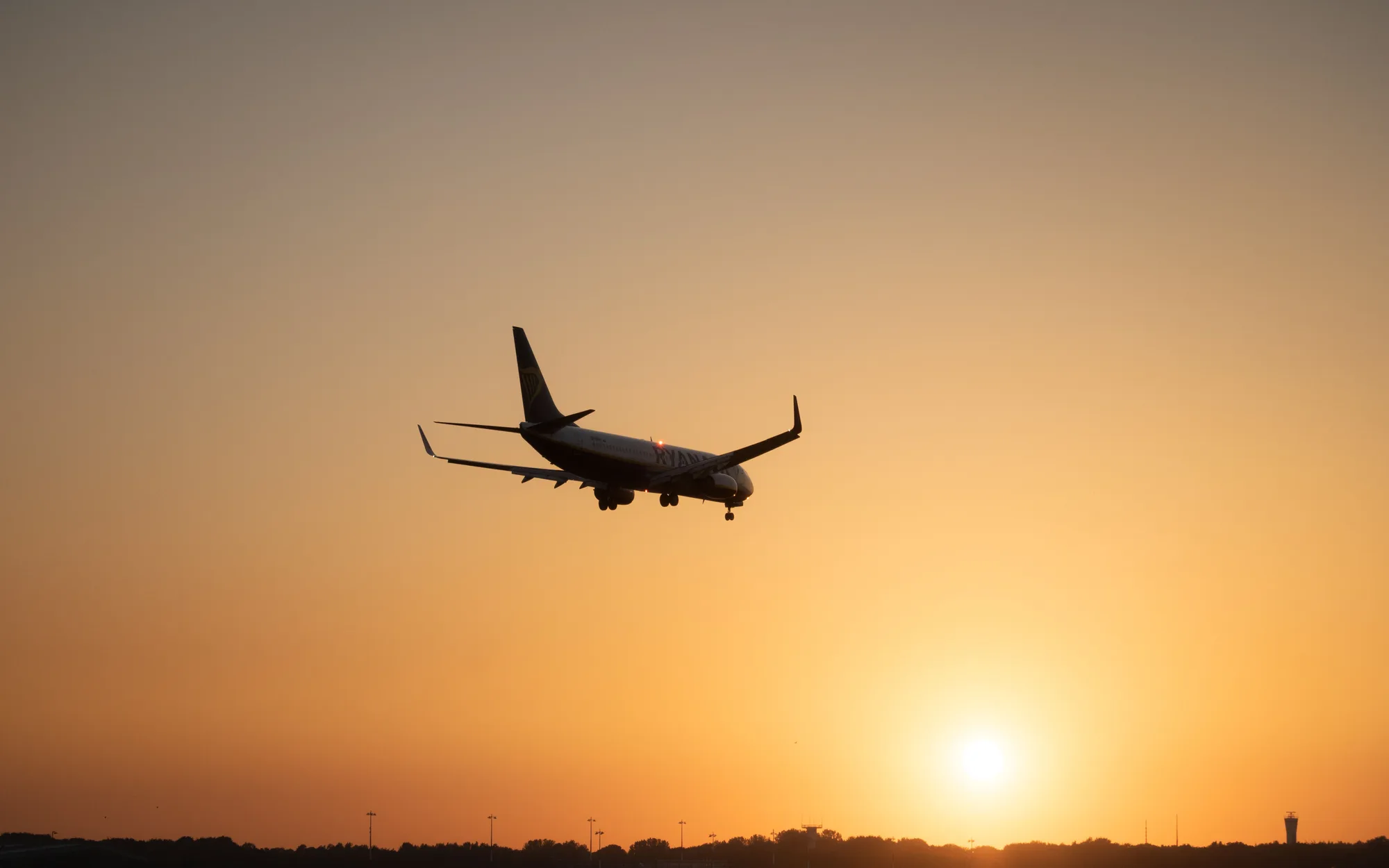 An airliner on approach, silhouetted against a low sun