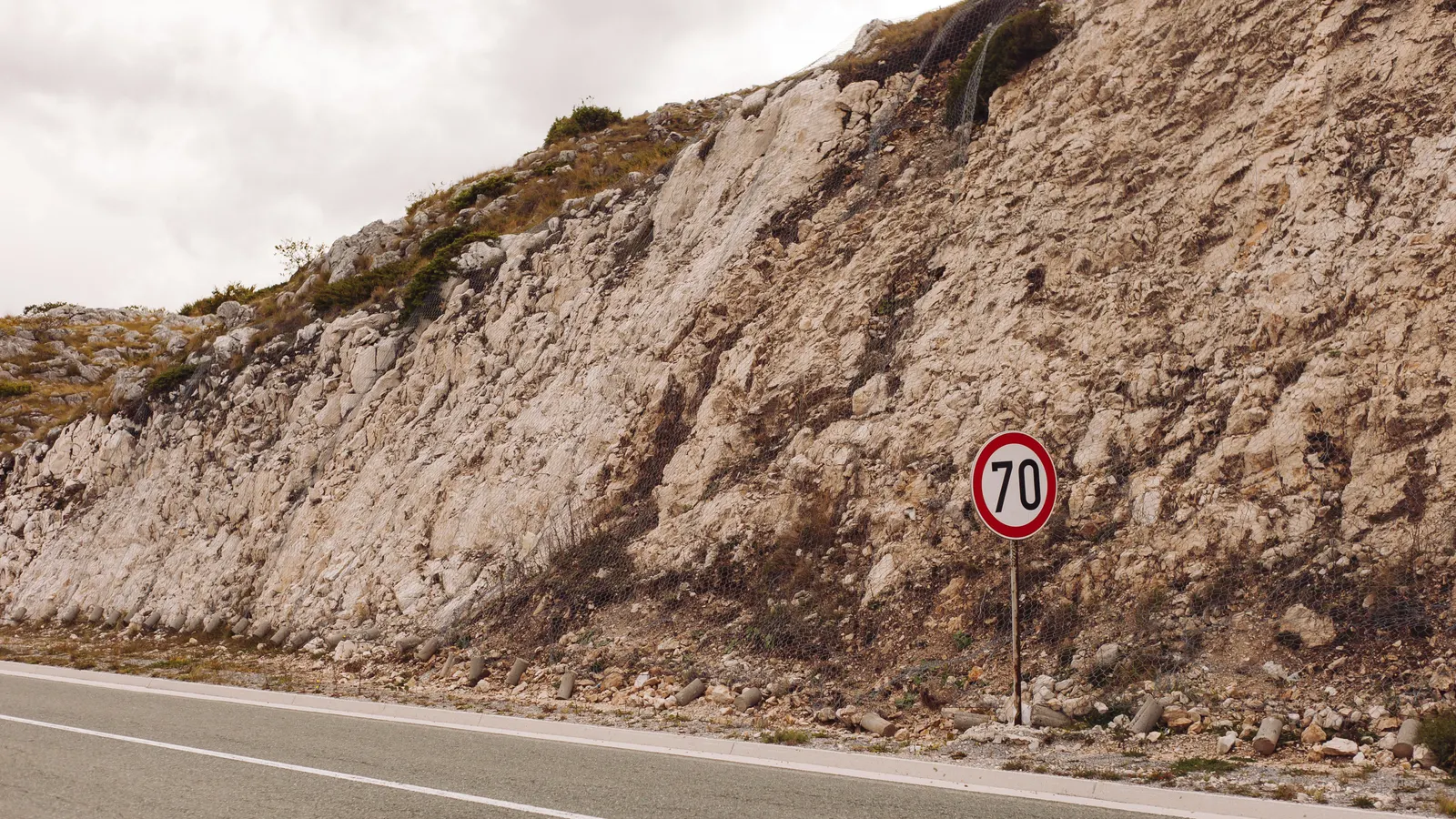 A speed limit sign against a cut limestone bank on an empty road